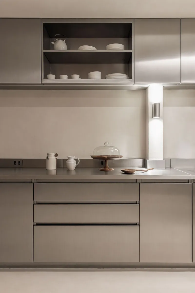 Stainless steel countertop with open shelving displaying ceramic vessels and a recessed task light
