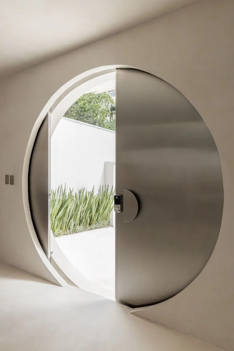 Circular pivot door with stainless steel panel opening to a planted courtyard with grasses