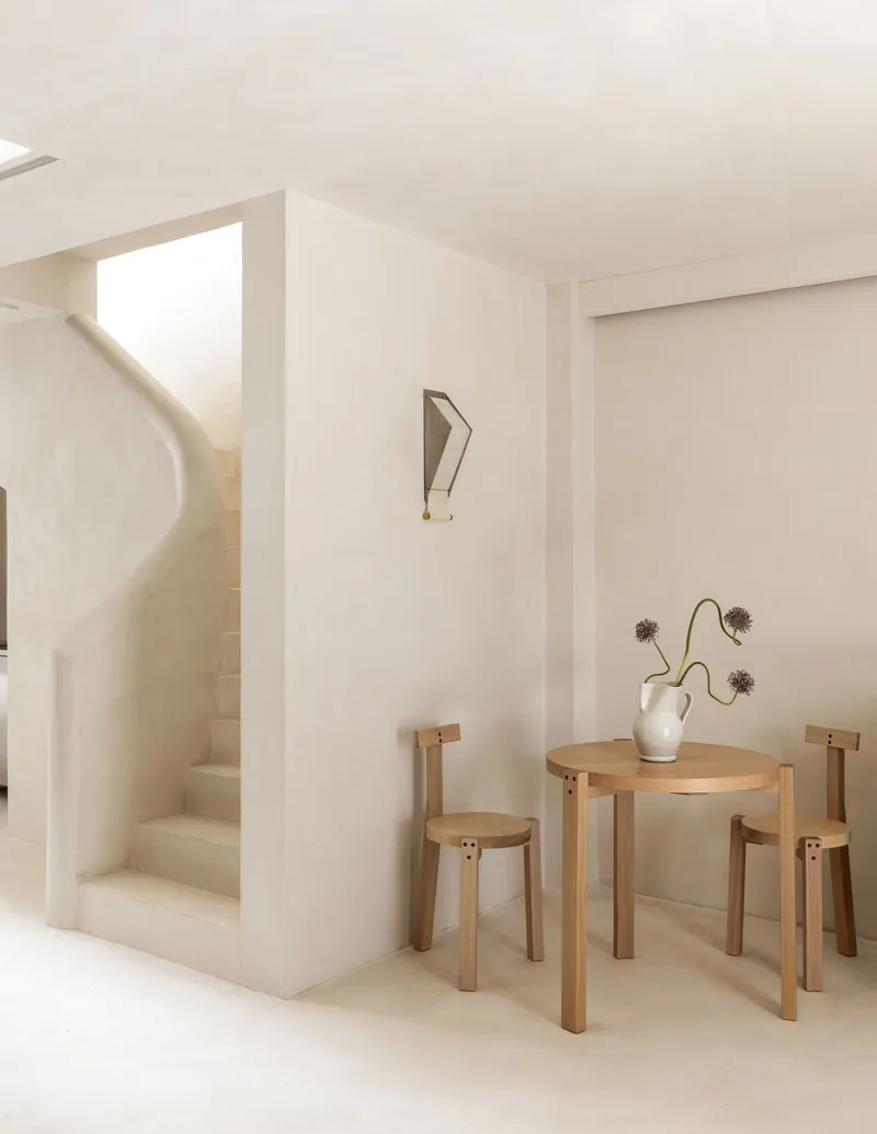 Rounded staircase beside a timber dining table with two stools and a vase of dried flowers