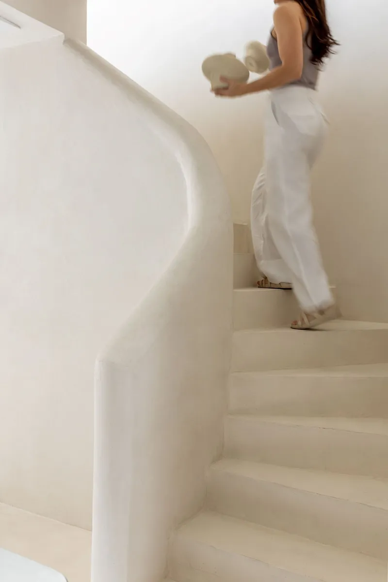 Curved plaster staircase with integrated handrail as a person ascends carrying a vase