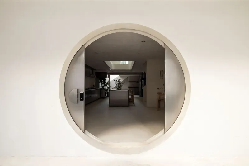 Circular plaster portal framing a view through to the kitchen and skylight beyond