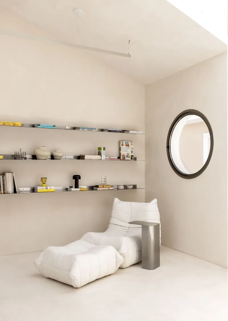 Corner nook with floating shelves and white lounge seating beneath a vaulted ceiling