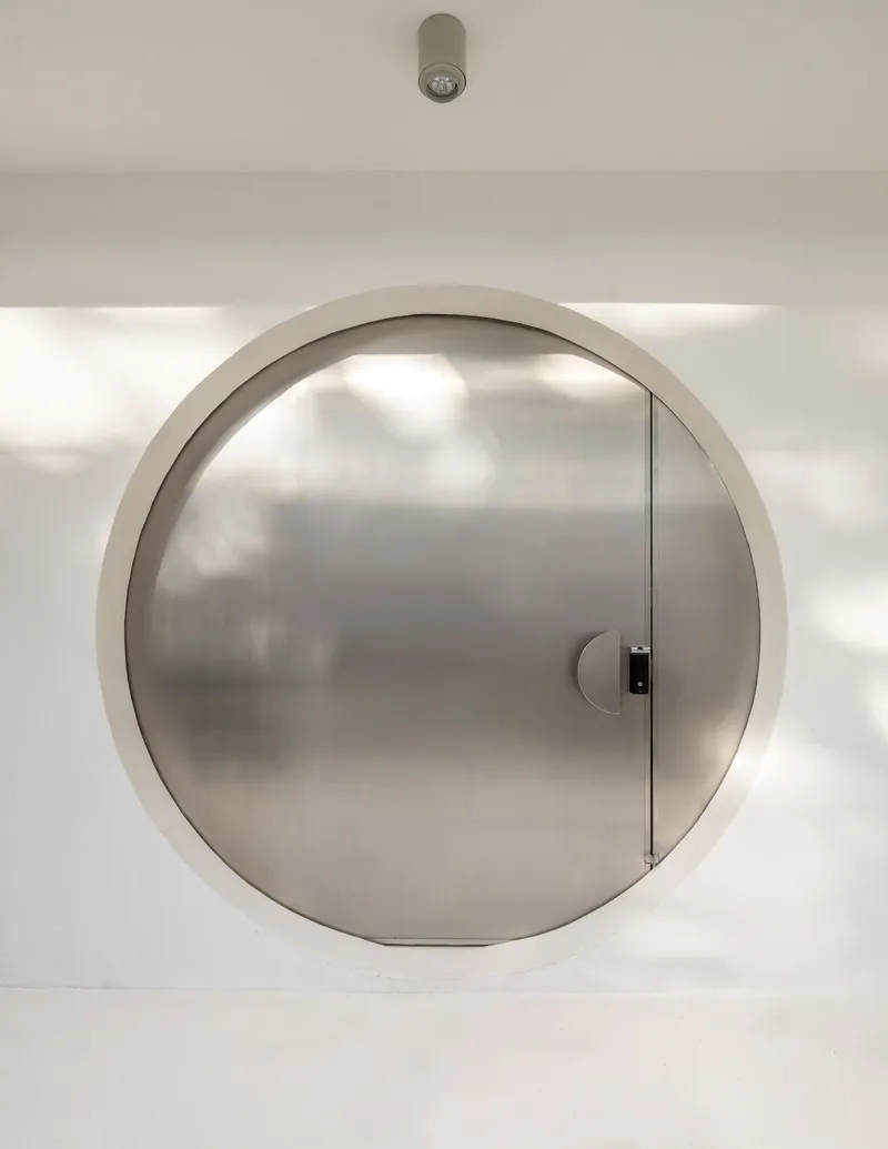 Closed circular stainless steel door set within white plastered wall