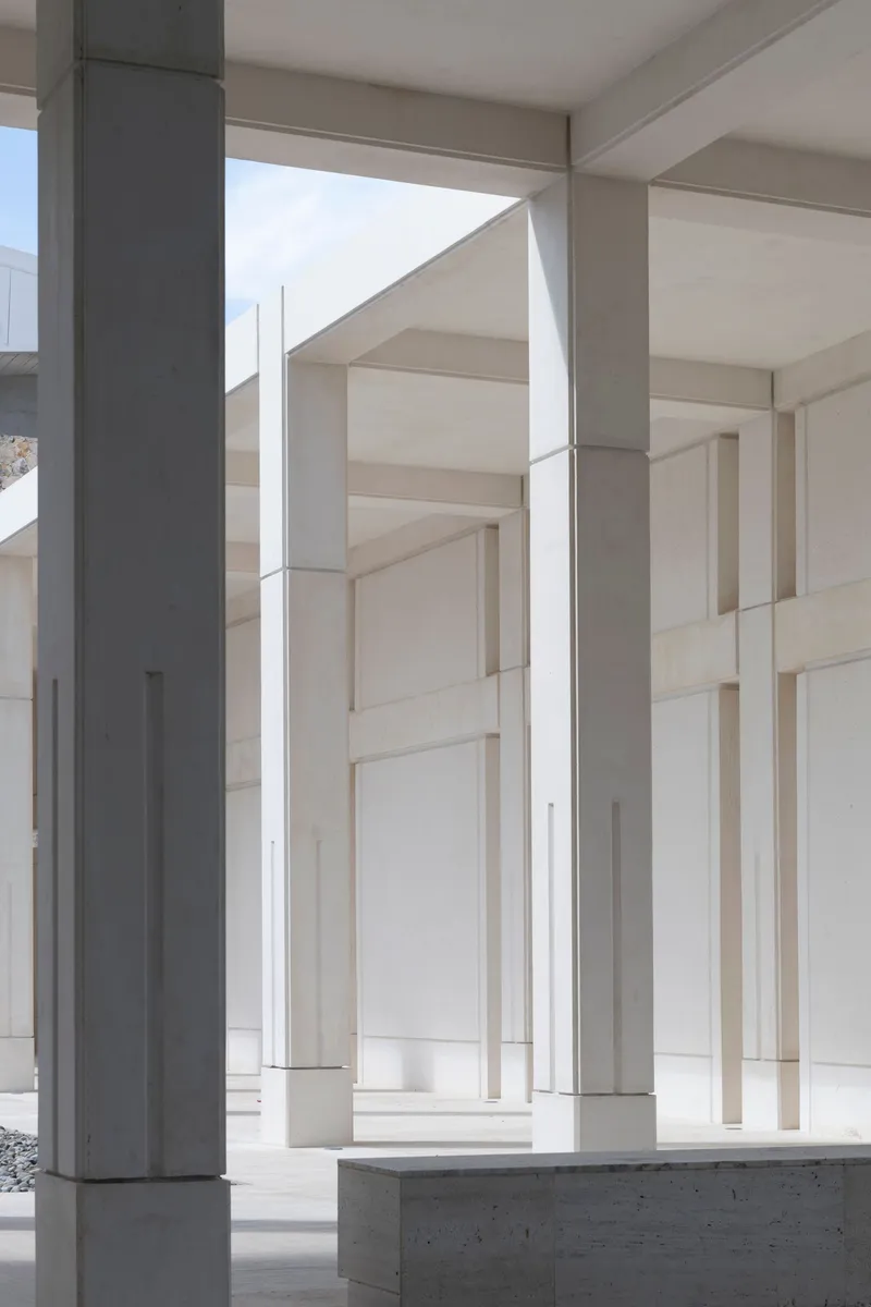 Colonnade of slender white concrete columns between cream-colored wall panels under bright daylight