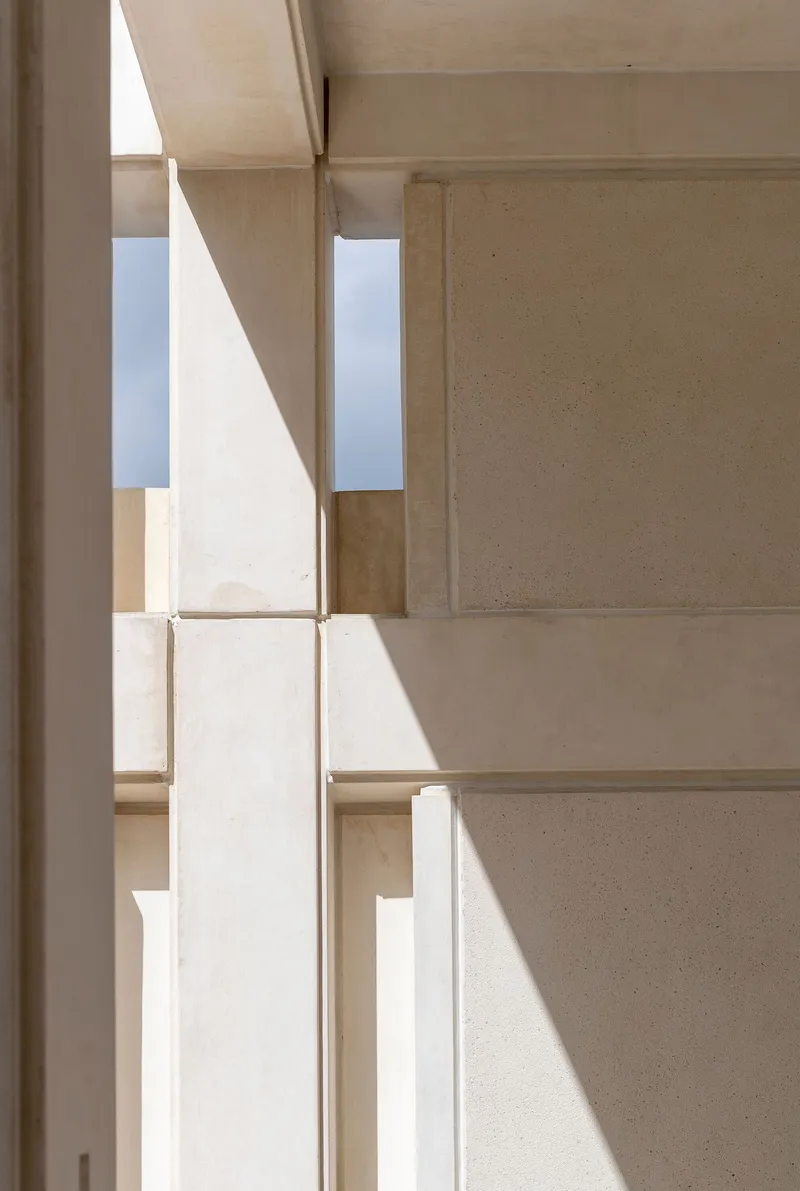 Vertical slot window casting angular sunlight across layered concrete wall surfaces