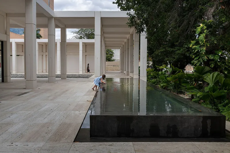 Colonnade courtyard with raised reflecting pool bordered by tropical plantings and a child at the water's edge