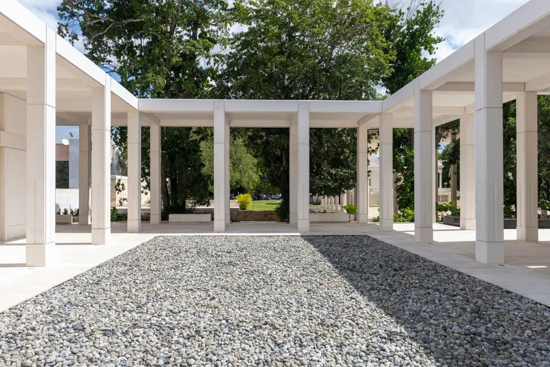 Open-air pavilion with white columns framing gravel courtyards and mature trees beyond