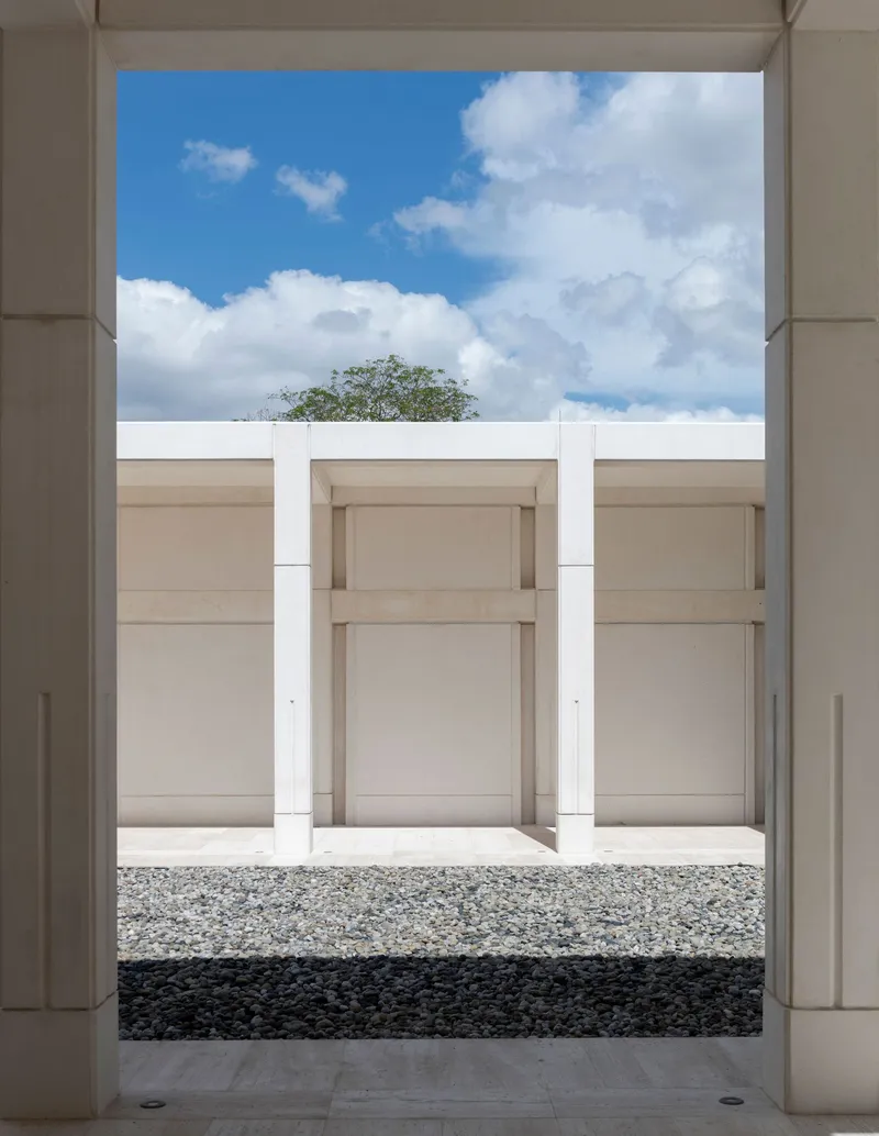 View through portico framing three recessed wall niches with gravel floor and blue sky above