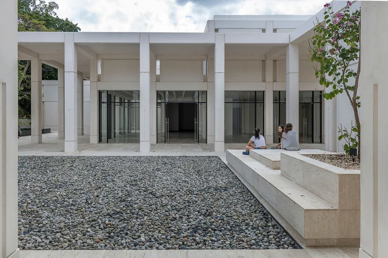 Courtyard with gravel bed and concrete planter bench where two visitors sit beneath a colonnade