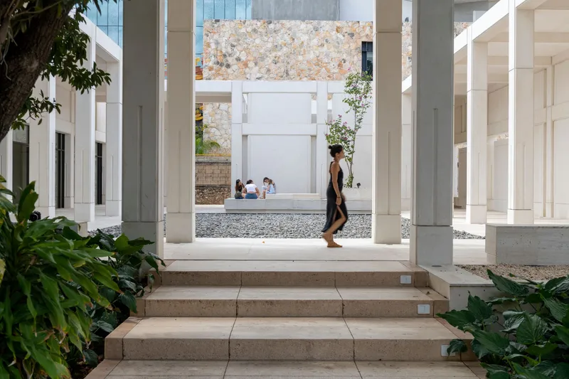 Stone steps leading through white columns as a visitor walks past gravel courtyards and planted trees