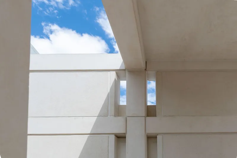 Upward view of stacked concrete slabs and column creating geometric shadows under blue sky