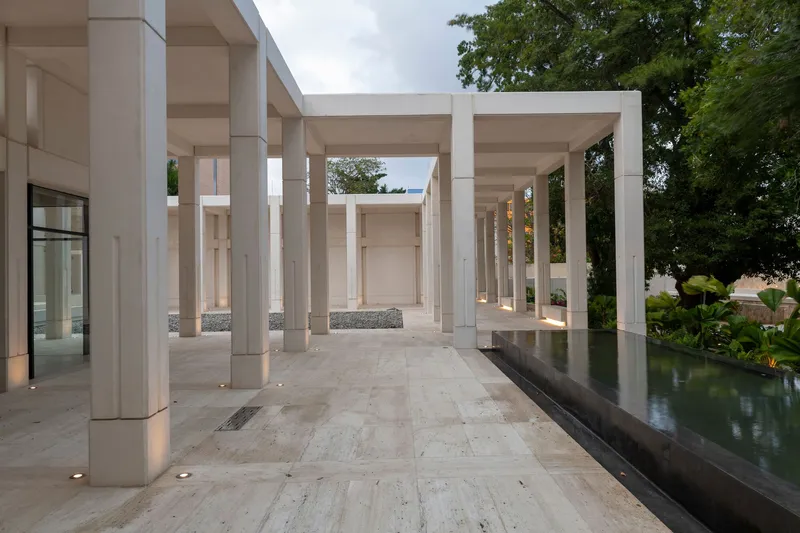 Covered colonnade with stone pavers alongside a reflecting pool at dusk with lotus plants visible