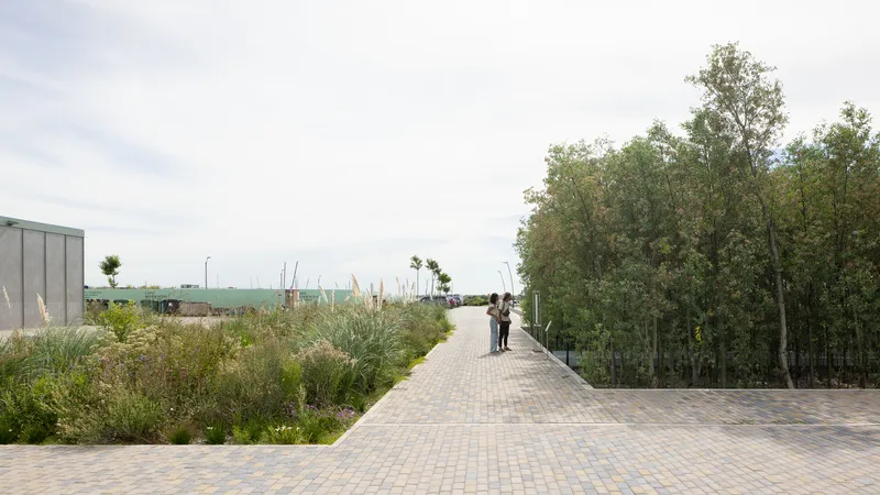 Brick paved terrace bordered by tall grasses with two figures walking toward distant woods