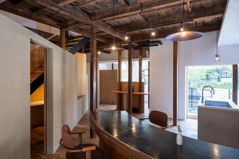 Open kitchen and dining area beneath exposed timber beams with pendant lights and doorway to terrace