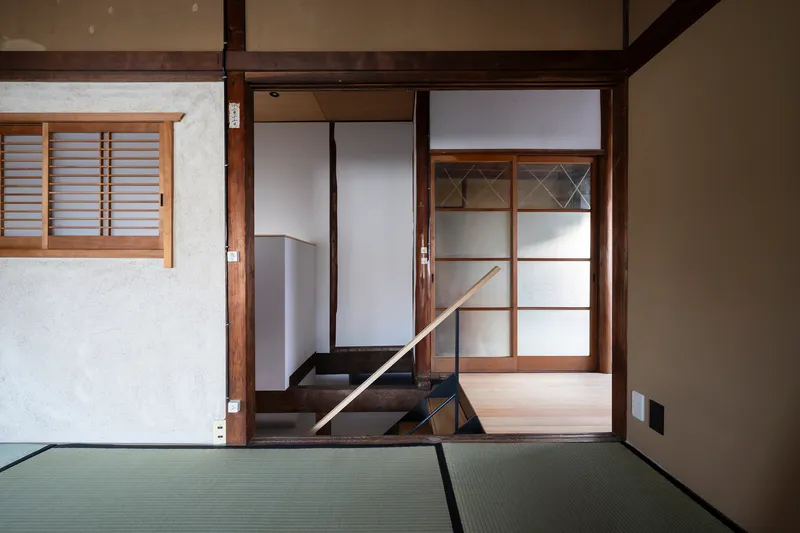 Tatami-mat room with sliding screen doors and glimpse of a steep stair beyond timber columns