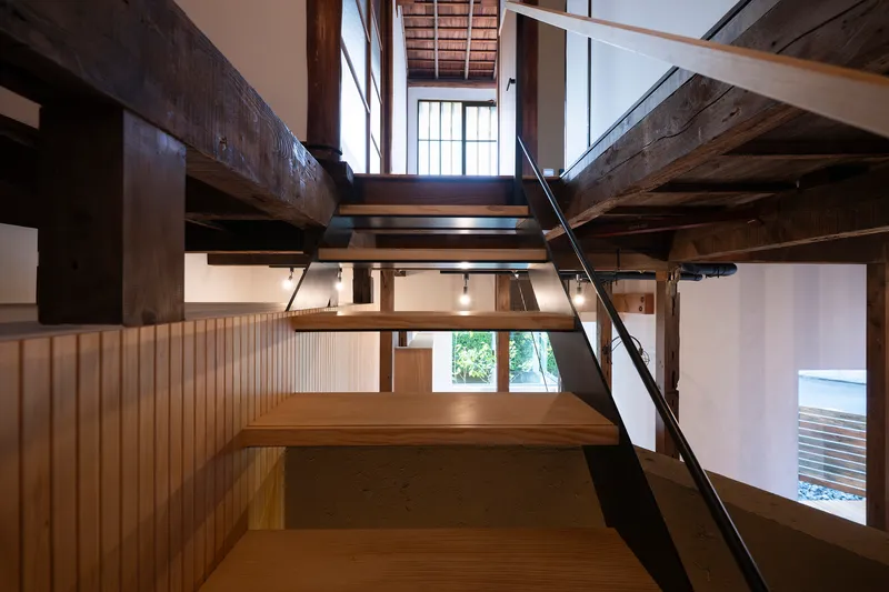Angled steel stair connecting split-level timber platforms beneath exposed structural beams and skylights
