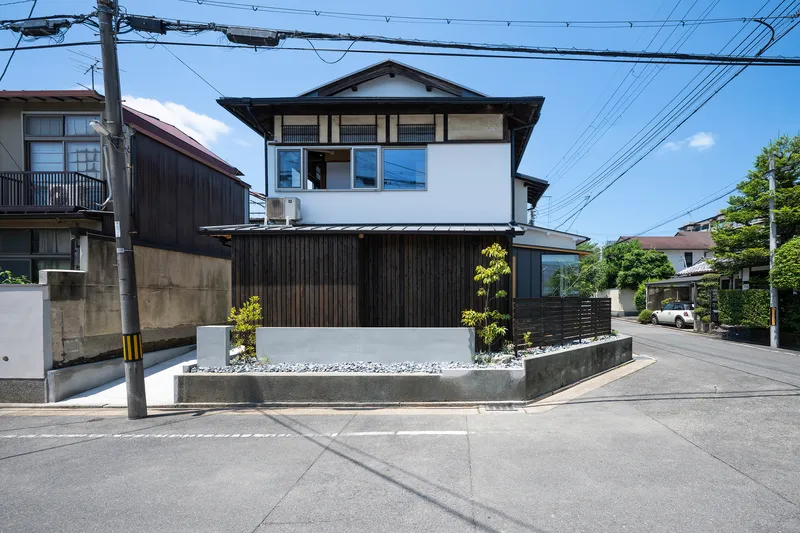 Two-story facade with white upper level and charcoal timber cladding at street level beneath overhead wires