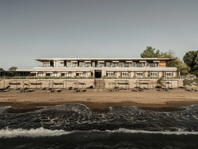 Two-story beachfront facade with horizontal balconies and timber cladding viewed from the water's edge