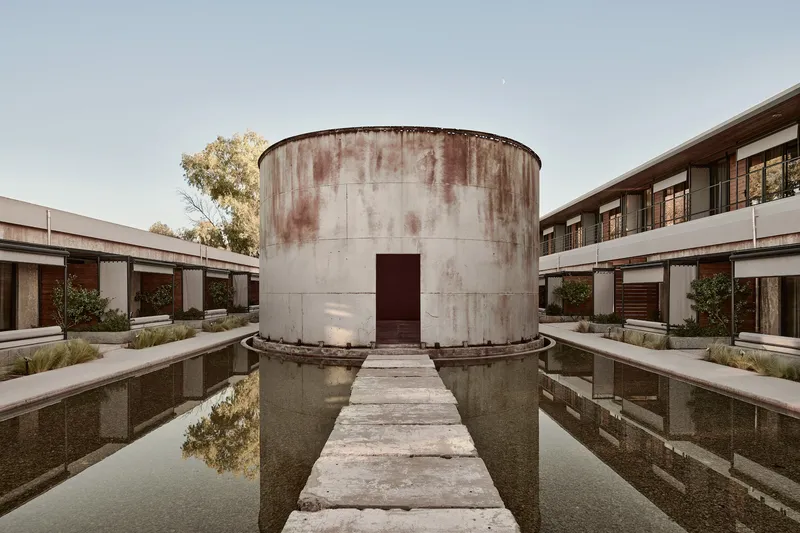 Weathered concrete cylinder with narrow walkway crossing a shallow reflecting pool in the central courtyard