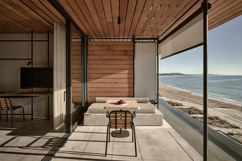 Living area with concrete flooring and full-height glazing framing the beachfront and distant hills