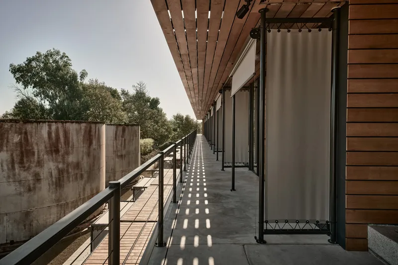 Corridor with slatted timber overhang casting patterned shadows beside a weathered concrete wall