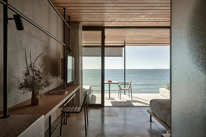 Interior living space framed by concrete walls with glazed doors opening to ocean terrace