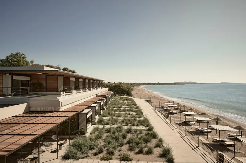 Linear beachfront facade with timber cladding and planted dune grasses along sandy shore