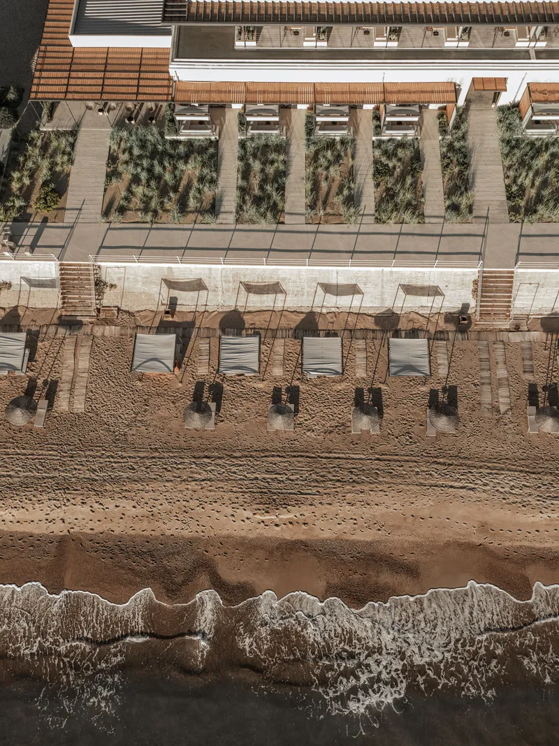 Aerial view of timber cabanas and planted terrace beds between beach and building edge