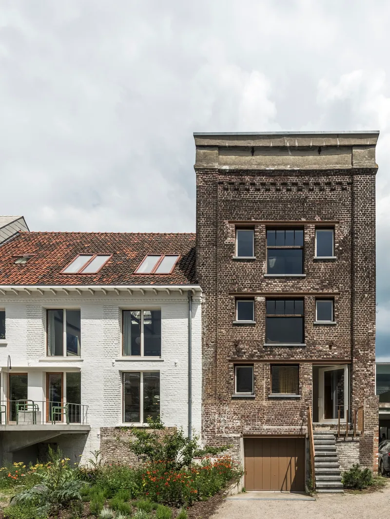 Street view showing dark brick tower adjoining a white-painted brick volume with terracotta tile roof