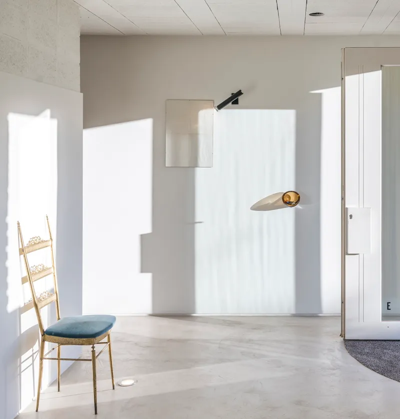 Interior room with concrete floor, timber ladder chair and sharp sunlight patterns across white walls