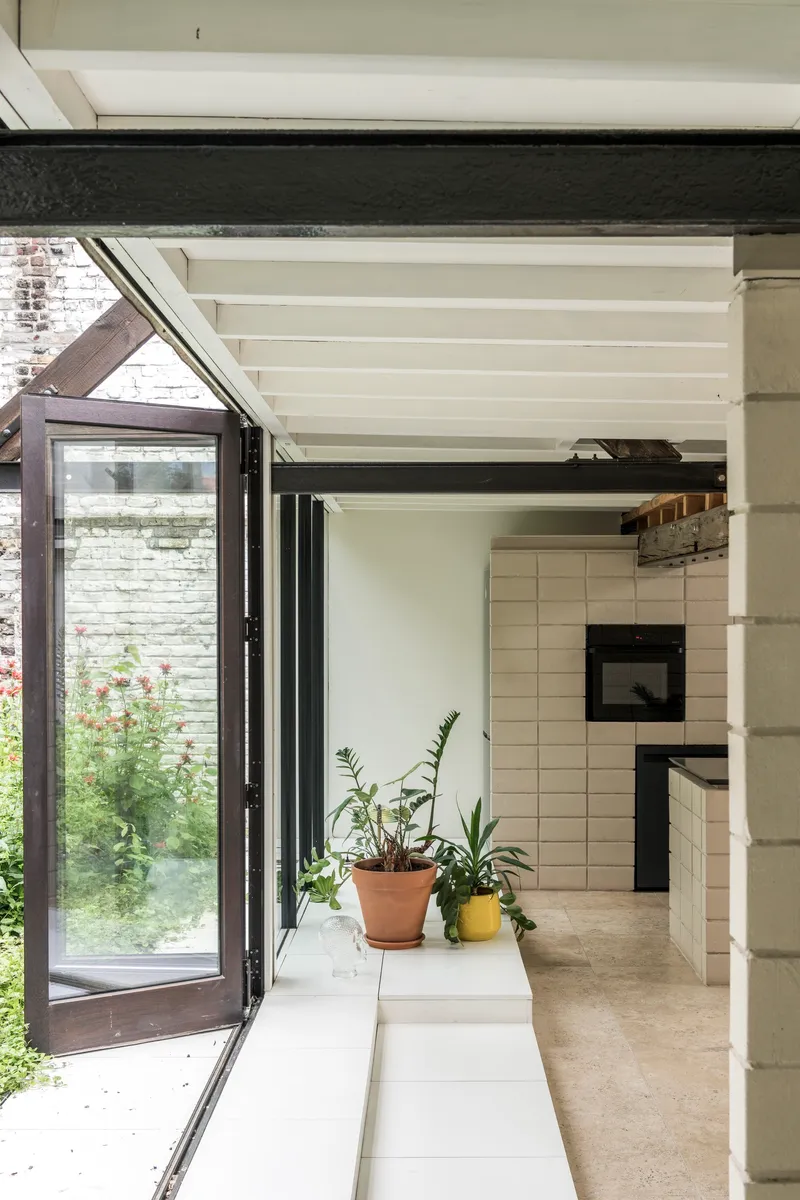 Open folding glass door leading to a planted courtyard with potted plants on the interior sill