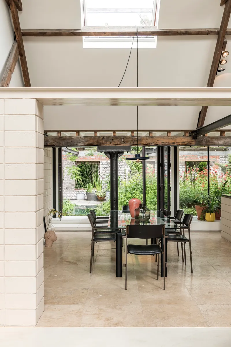 Dining area with exposed timber beams and steel structure overlooking a garden through floor-to-ceiling glazing
