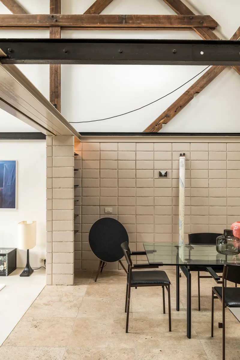 Cream rectangular tile wall with exposed timber roof trusses and steel beams overhead