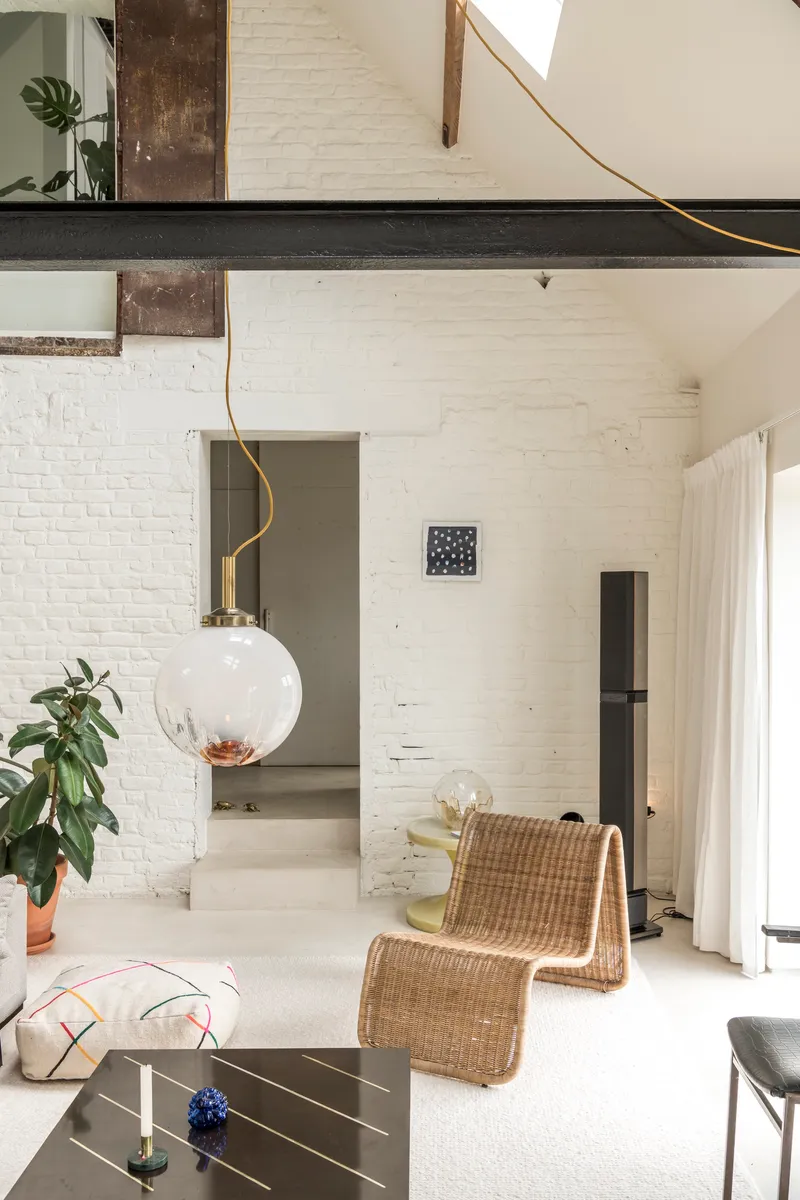 Double-height living space with exposed white brick walls, dark structural beam, and spherical pendant light