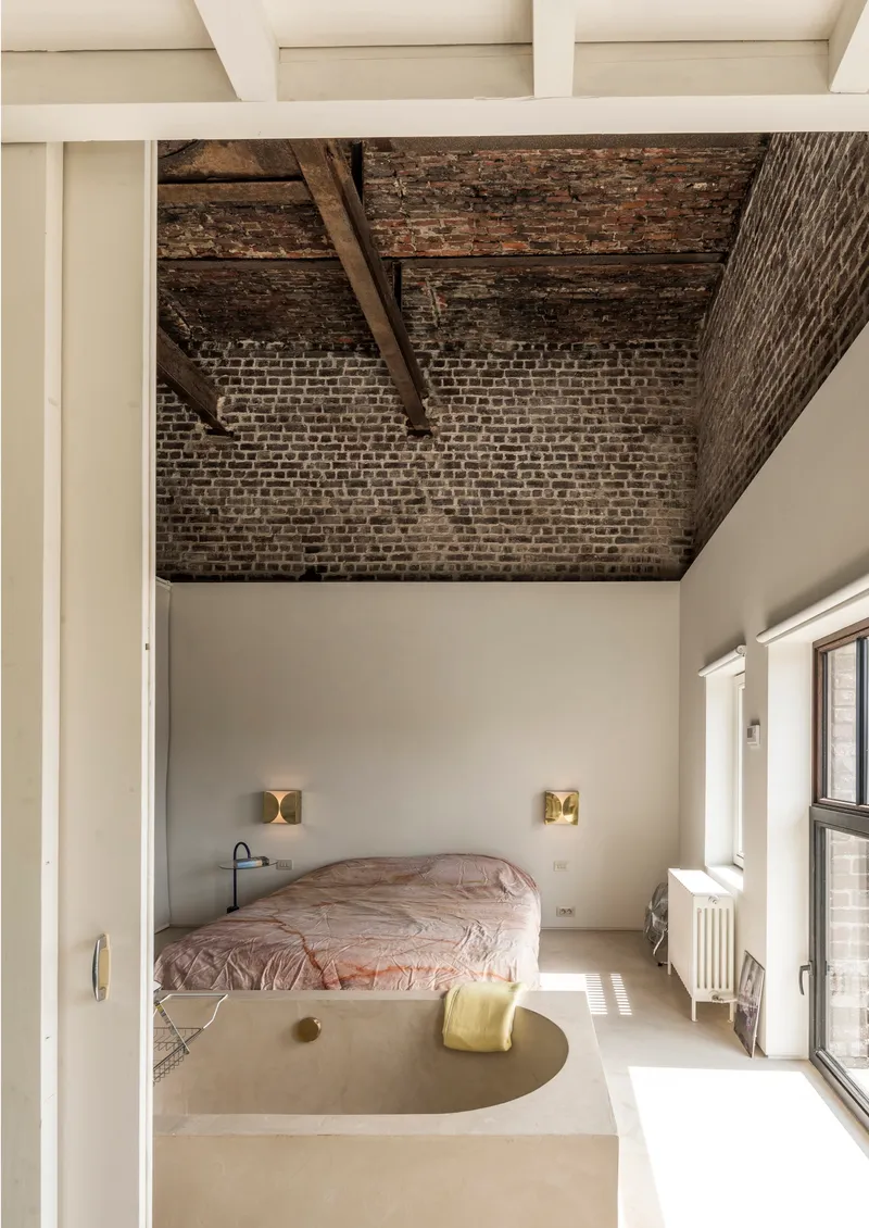 Bedroom with exposed brick ceiling vault, timber beams, and raised platform bed framed by white walls