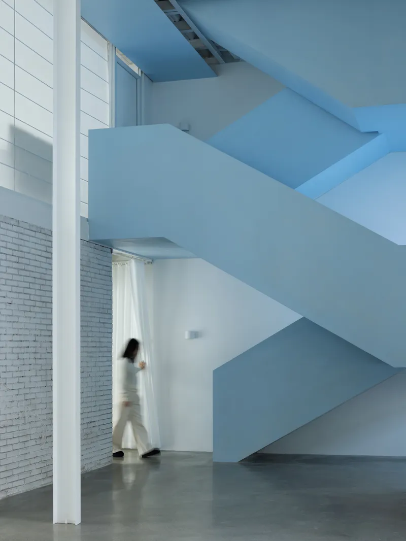 Cantilevered blue staircase with a figure in motion passing beneath the folded geometry