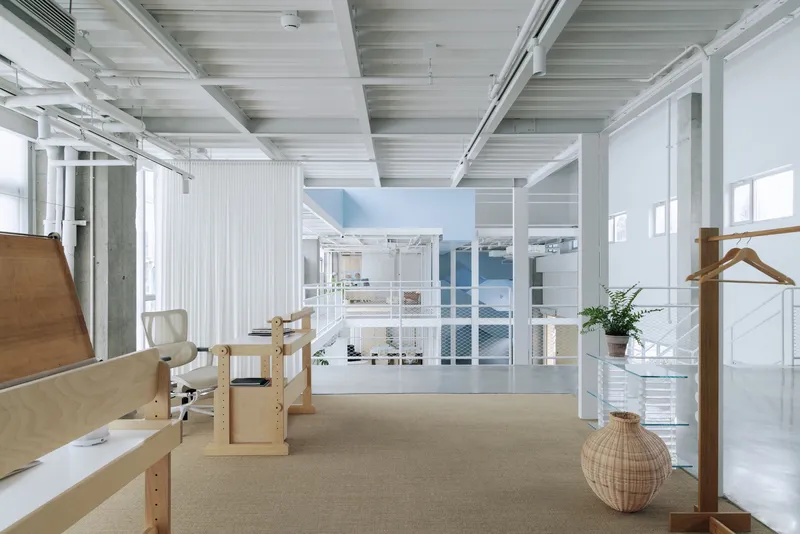 Open workspace interior with exposed white ceiling beams and translucent curtain partitions dividing the space
