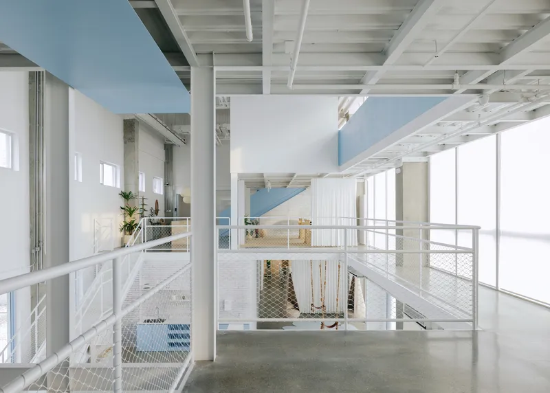 Double-height interior with white metal mesh railings and exposed timber joist ceiling over polished concrete floors