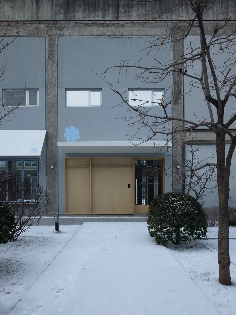 Entrance with light wood sliding doors framed by concrete columns and bare winter trees in snow