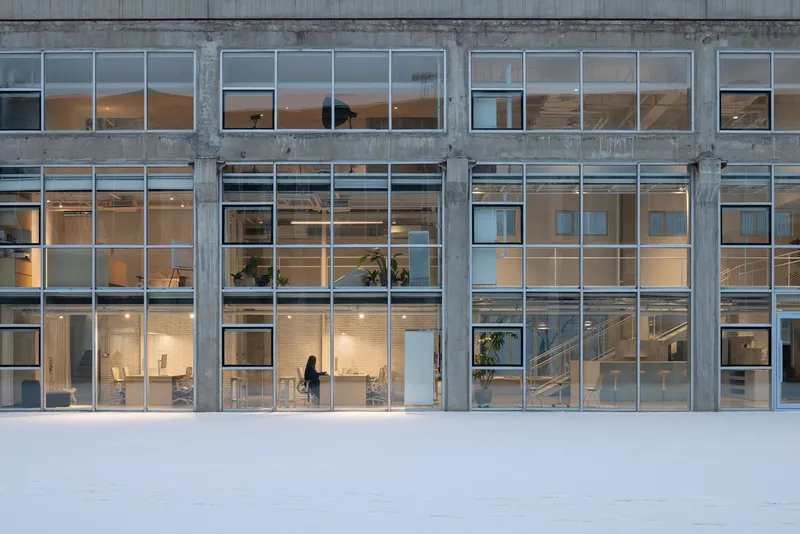 Glass and concrete facade with gridded windows overlooking a snow-covered courtyard at dusk