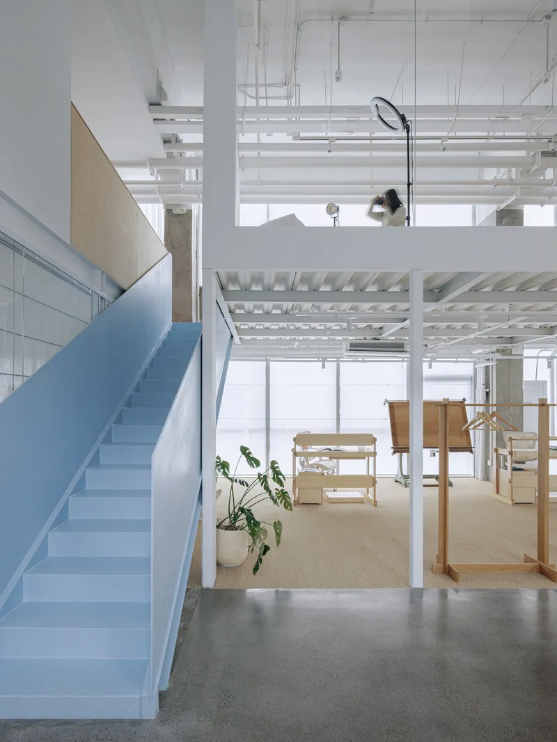Interior view of pale blue staircase with exposed ceiling infrastructure and potted plant below