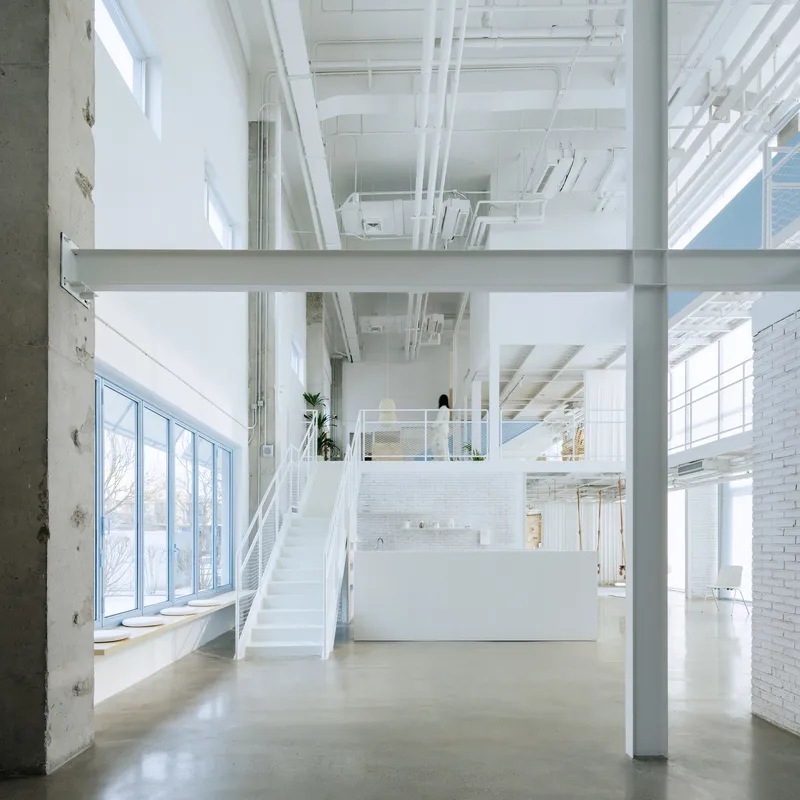 Double-height interior with white steel stair connecting mezzanine levels under exposed mechanical systems