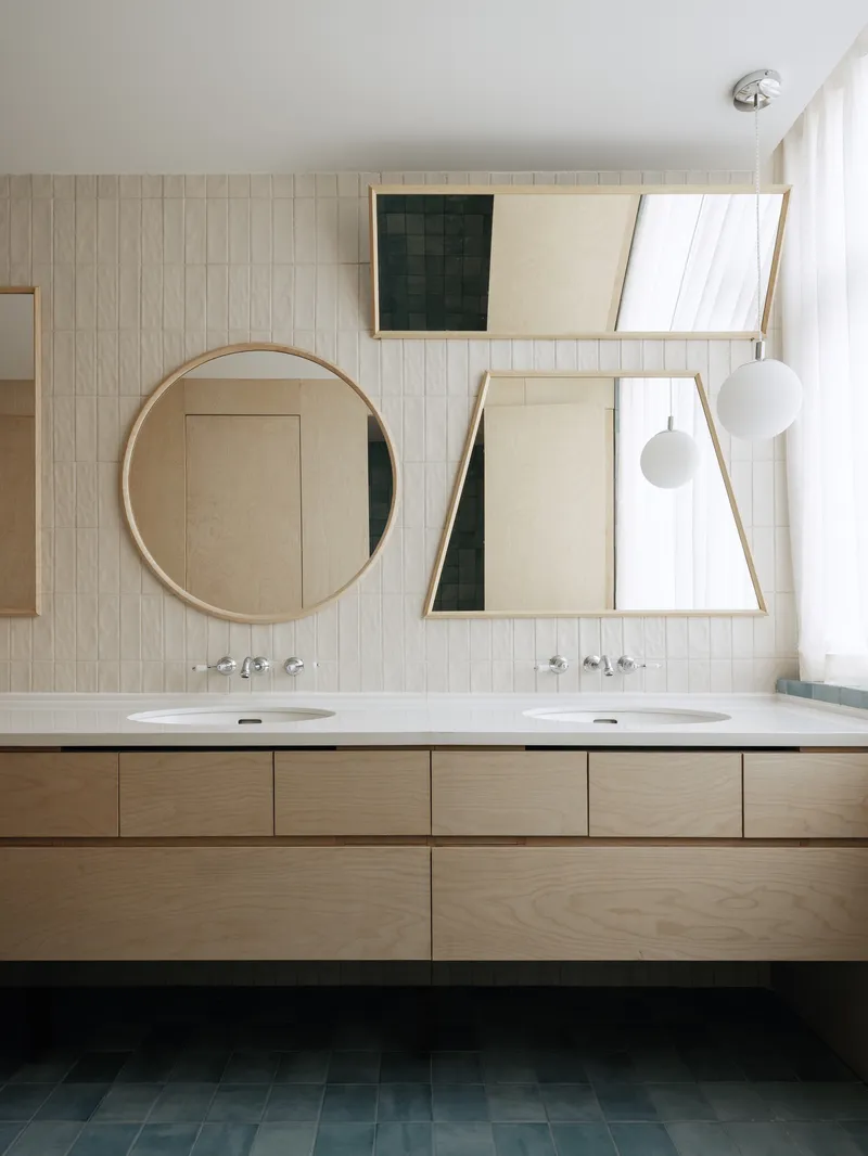 Bathroom vanity with dual sinks beneath round and angled mirrors against vertical tile wall