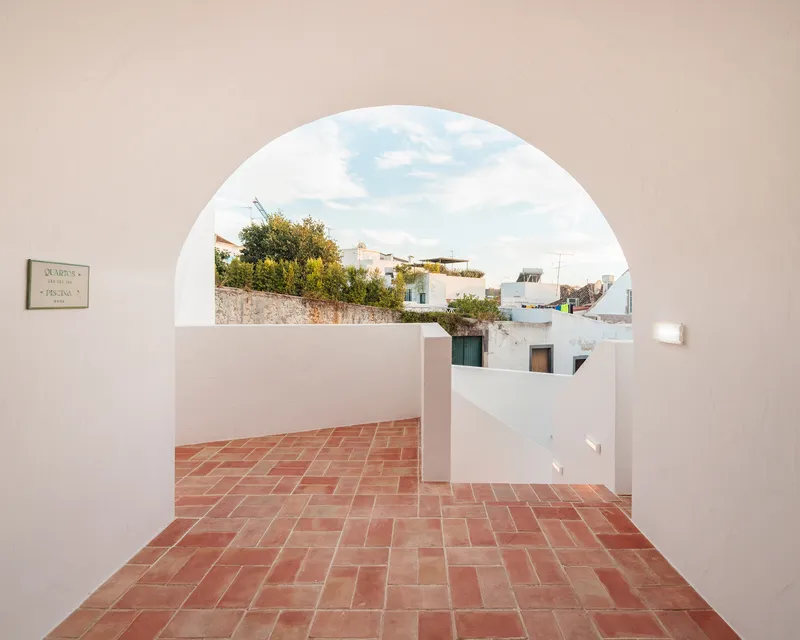 Terracotta-paved terrace framed by an arched opening overlooking neighboring white buildings and trees