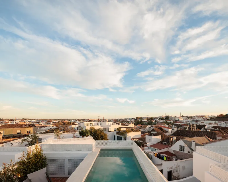 Rooftop pool with perforated white screening overlooking terracotta rooftops at dusk
