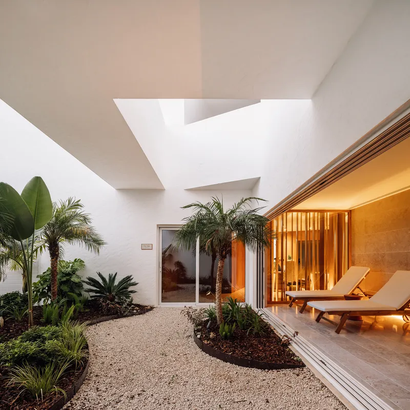 Interior courtyard with gravel pathways, tropical palms, and timber-screened spa room illuminated at dusk