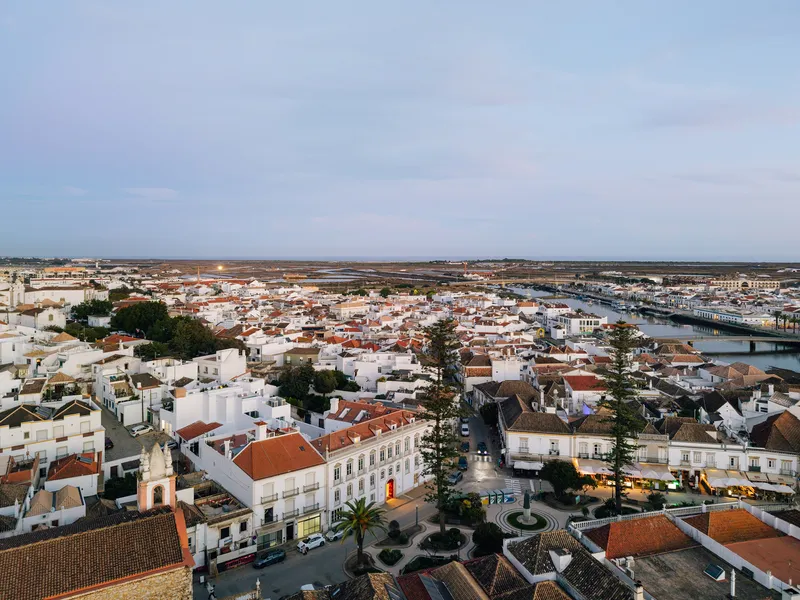 Aerial view of whitewashed rooftops and terracotta tiles spreading toward distant wetlands under evening light