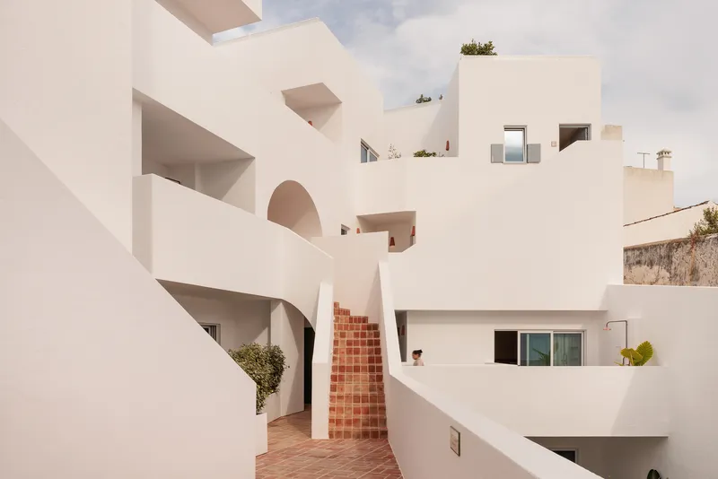 Courtyard with white stucco volumes, recessed arched openings, terracotta brick stair and scattered planters