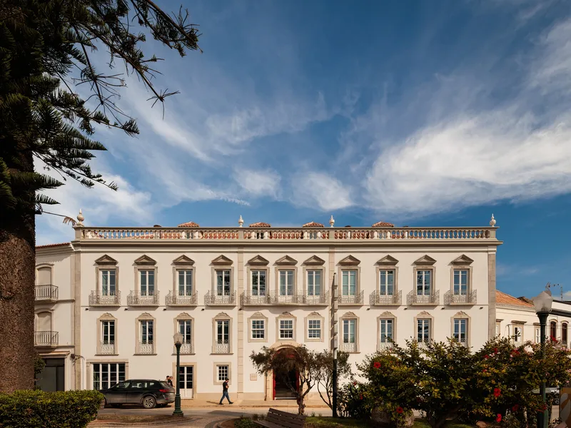Street facade with symmetrical window openings, balustraded roofline and palm tree framing the view