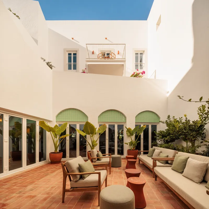 Interior courtyard with green-tiled arched openings, terracotta paving and potted banana plants under a blue skylight